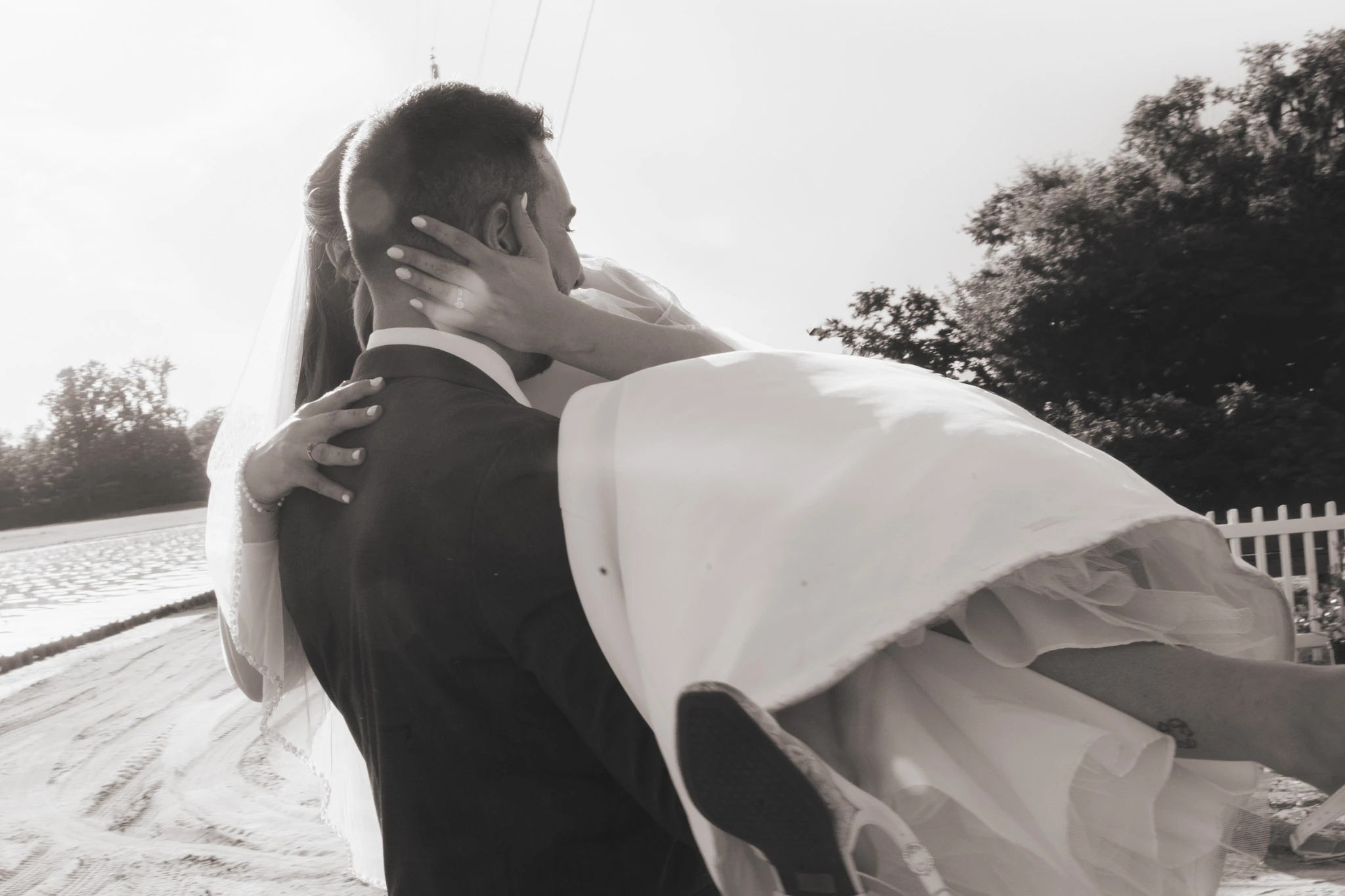 In sepia, the groom carries the bride, her dress spilling over his arm