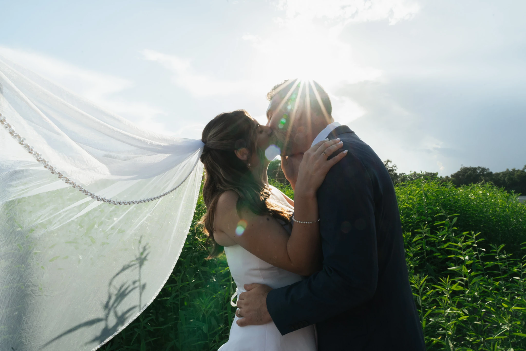 The veil streams out in the wind as the couple kiss into the sun