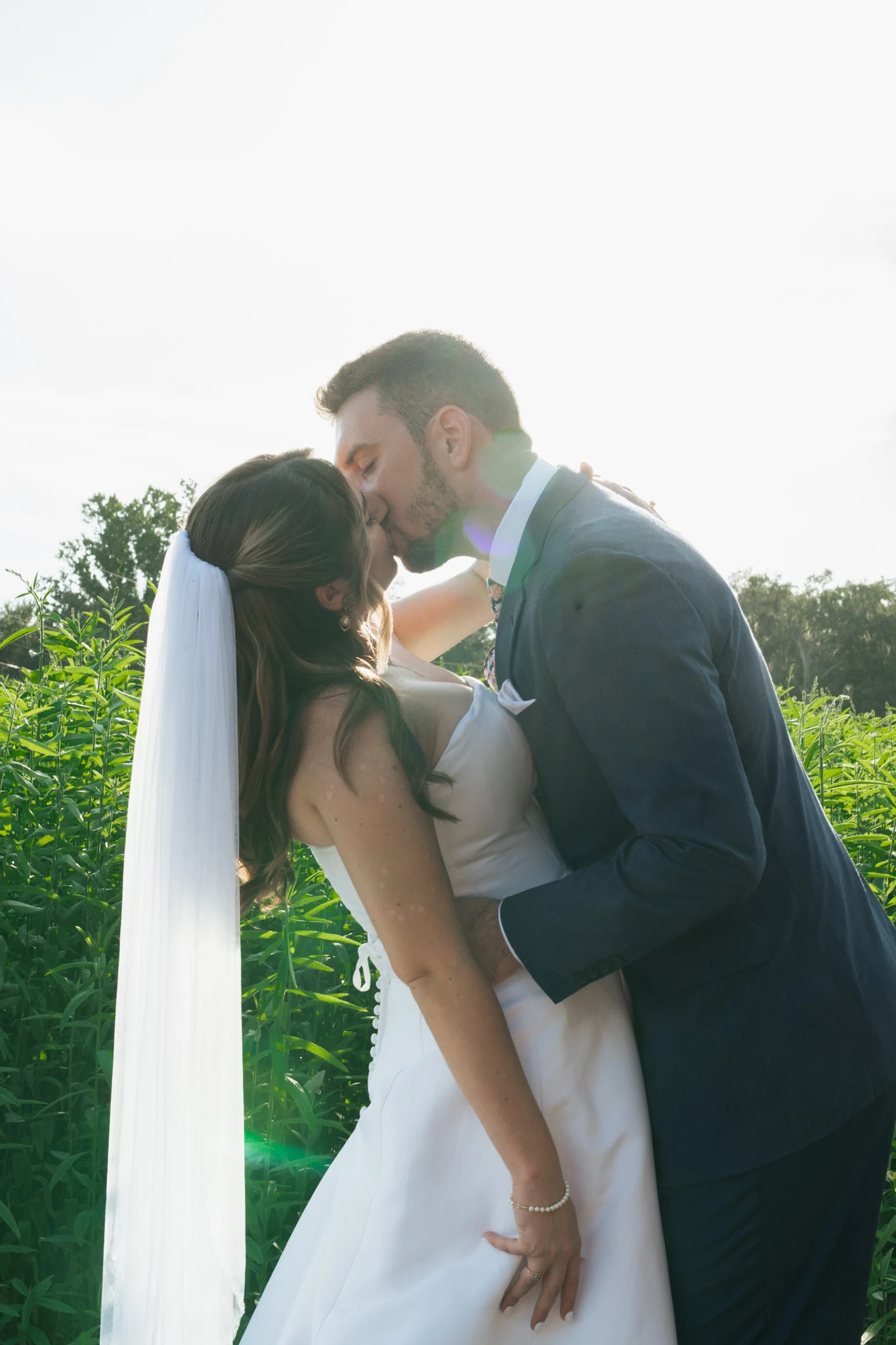 The groom dips the bride for a kiss in front of a tall green field
