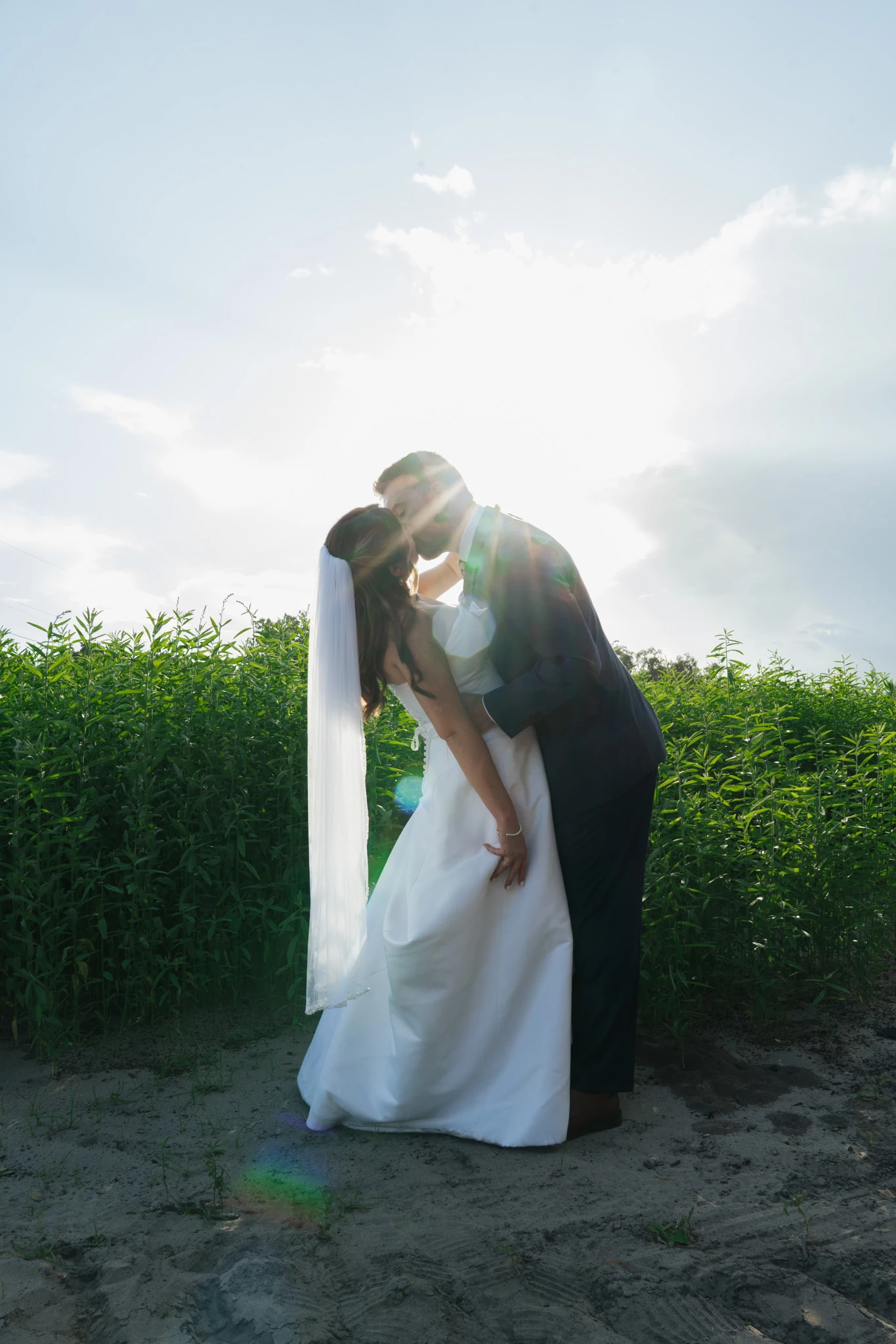 Wide, the dip kiss in silhouette with the sun behind them